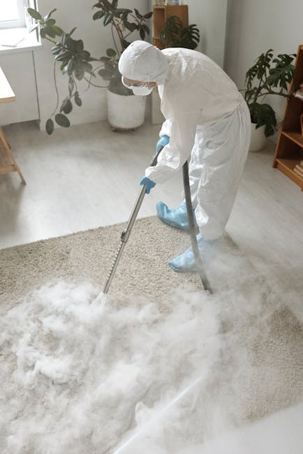 A woman using a yellow canister vacuum cleaner to perform surface cleaning and deep cleaning on a patterned area rug in a living room. The rug has intricate floral designs in shades of beige, green, a